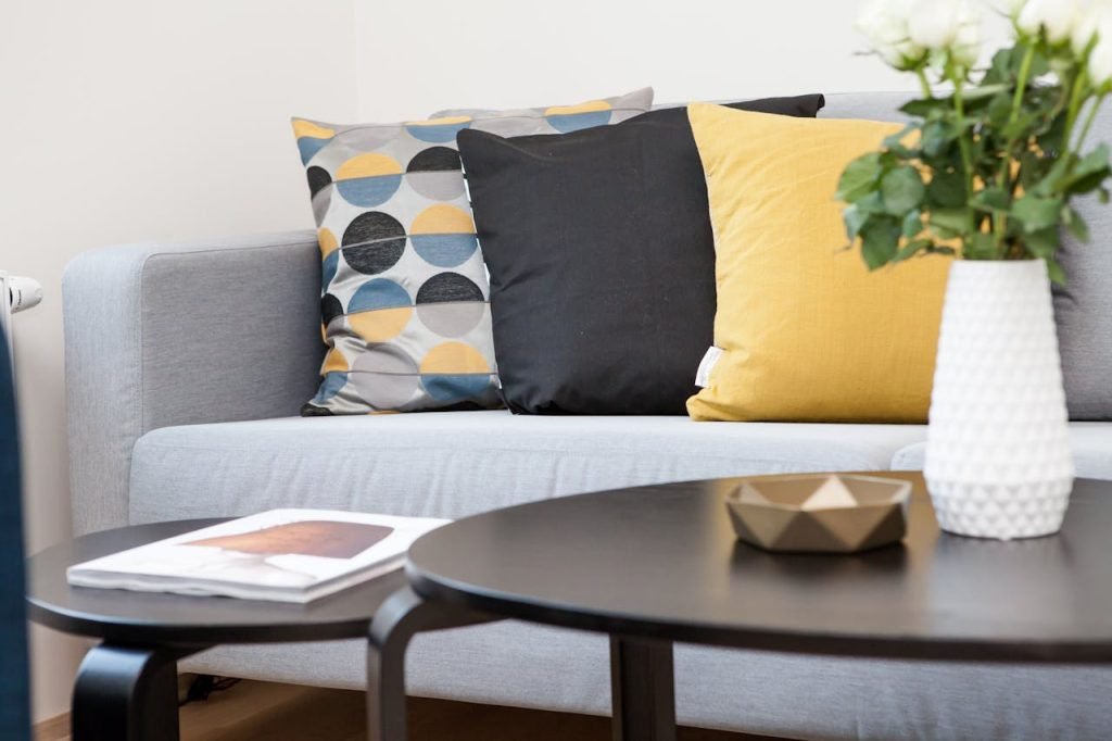 centerpiece-on-coffee-table-beside-sofa-with-three-pillows-298842 Contemporary living room interior featuring a stylish sofa, decorative pillows, and a vase of flowers.